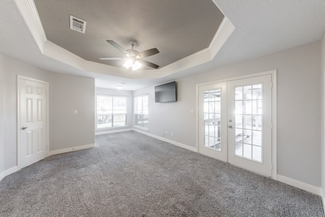 empty room featuring a raised ceiling, crown molding, french doors, and carpet