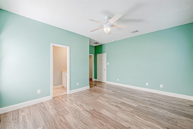 unfurnished bedroom featuring a textured ceiling, light wood-type flooring, ensuite bath, and ceiling fan