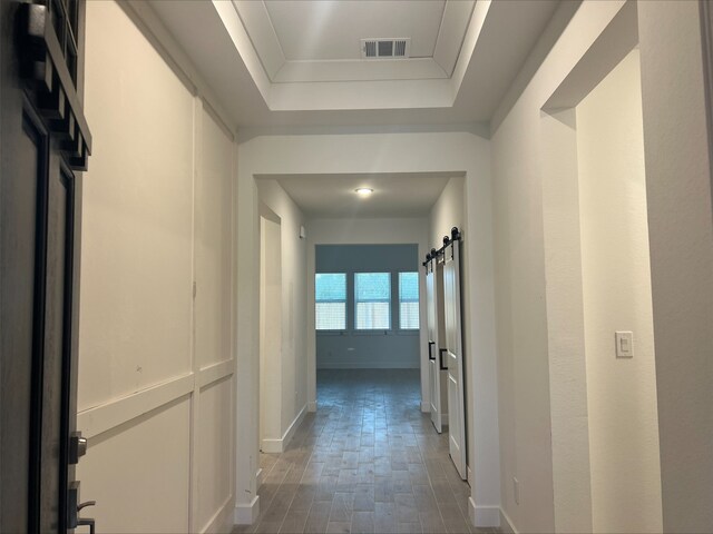 hallway with dark hardwood / wood-style flooring, a barn door, a raised ceiling, and crown molding