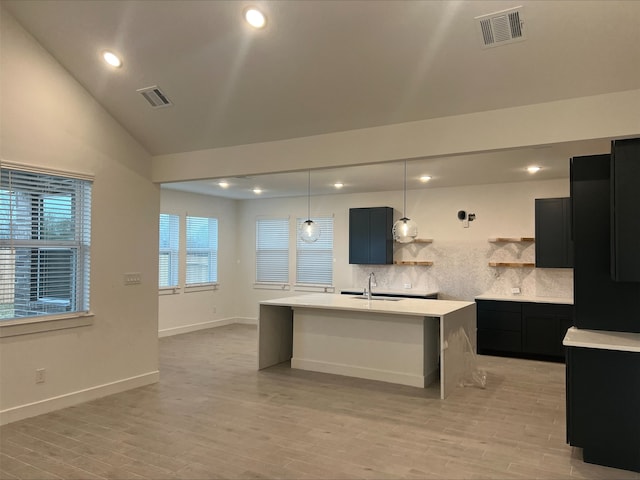 kitchen with sink, vaulted ceiling, decorative backsplash, an island with sink, and light hardwood / wood-style floors