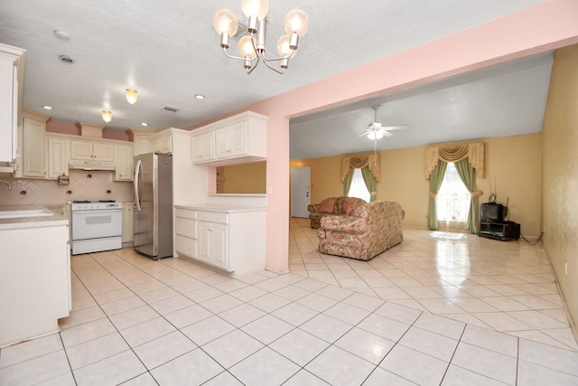 kitchen with gas range gas stove, sink, stainless steel fridge, light tile patterned floors, and ceiling fan with notable chandelier