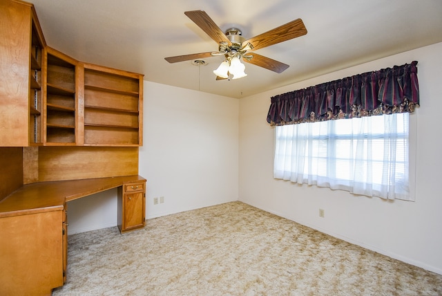 unfurnished office with ceiling fan, built in desk, and light carpet