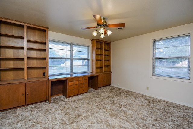 unfurnished office featuring ceiling fan, light colored carpet, and built in desk