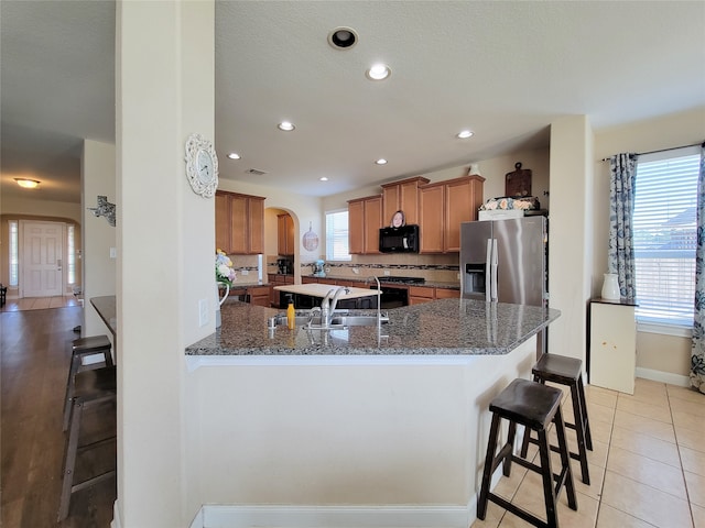 kitchen featuring a healthy amount of sunlight, a kitchen bar, stainless steel fridge with ice dispenser, and kitchen peninsula