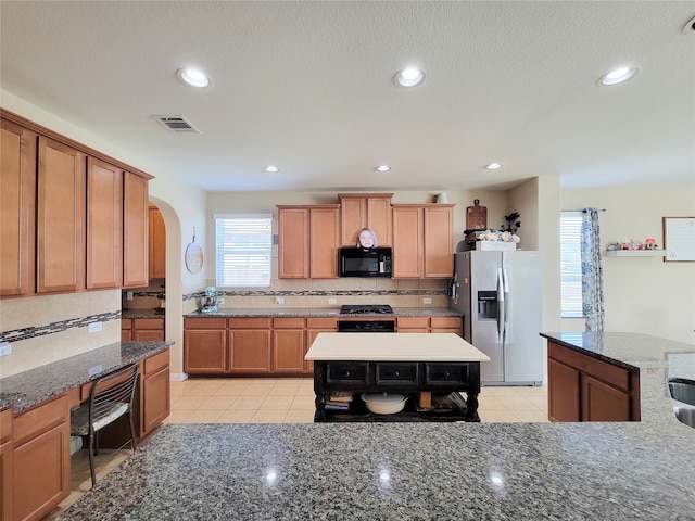 kitchen with tasteful backsplash, light tile patterned flooring, a kitchen island, and black appliances