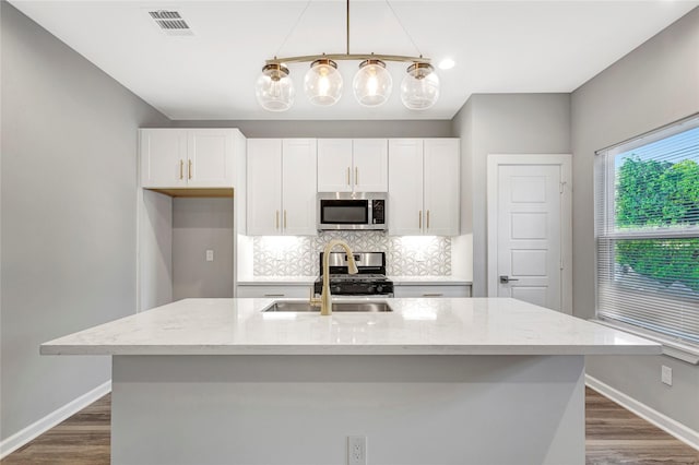 kitchen featuring pendant lighting, light stone counters, a center island with sink, and stainless steel appliances