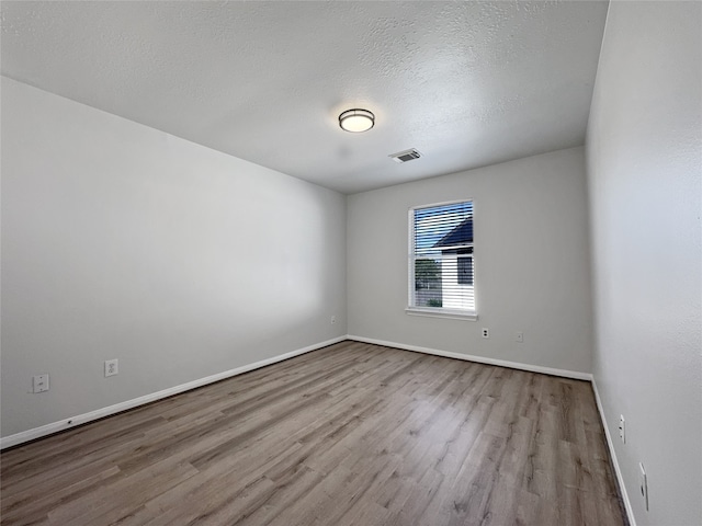 spare room with a textured ceiling and light hardwood / wood-style flooring