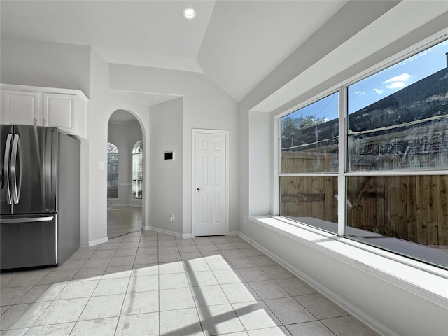 interior space featuring stainless steel refrigerator, light tile patterned floors, white cabinets, and vaulted ceiling