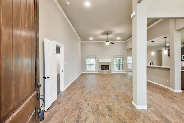 unfurnished living room featuring ceiling fan, sink, a stone fireplace, light hardwood / wood-style flooring, and crown molding