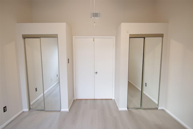 unfurnished bedroom with light hardwood / wood-style flooring and multiple closets