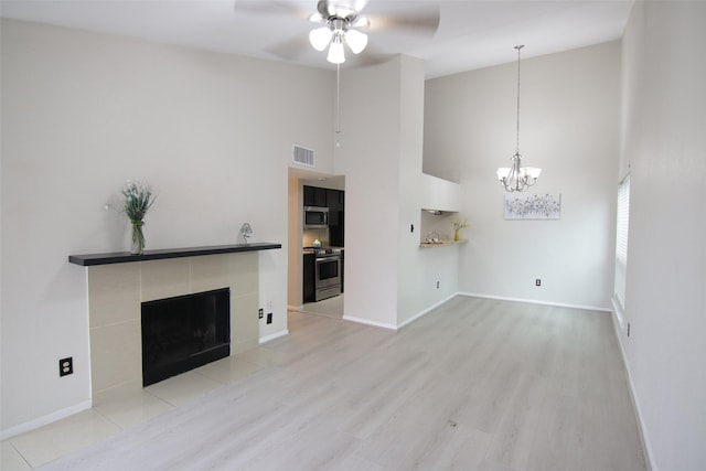 unfurnished living room with ceiling fan with notable chandelier, light hardwood / wood-style floors, a towering ceiling, and a tile fireplace