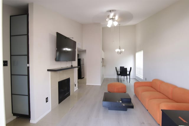 living room featuring ceiling fan with notable chandelier, a fireplace, and light hardwood / wood-style flooring