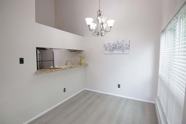 unfurnished dining area with a chandelier, a high ceiling, and light wood-type flooring