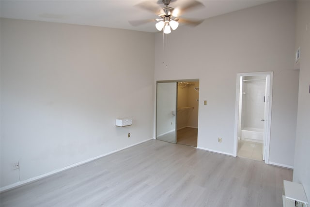 unfurnished bedroom with connected bathroom, ceiling fan, a towering ceiling, a walk in closet, and light wood-type flooring