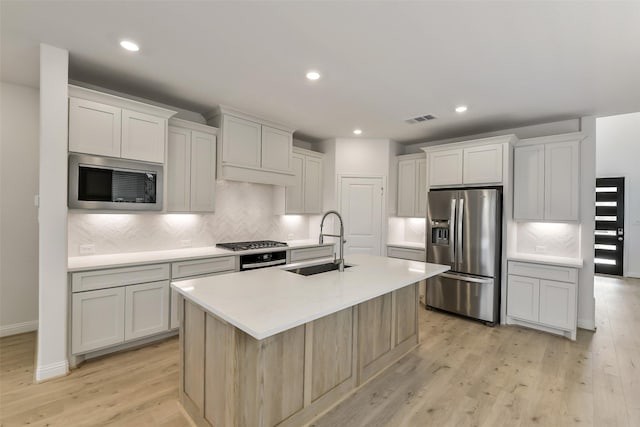 16334 Placid Stream St, Conroe, TX 77302 - kitchen featuring tasteful backsplash, a sink, an island with sink, light wood finished floors, and appliances with stainless steel finishes
