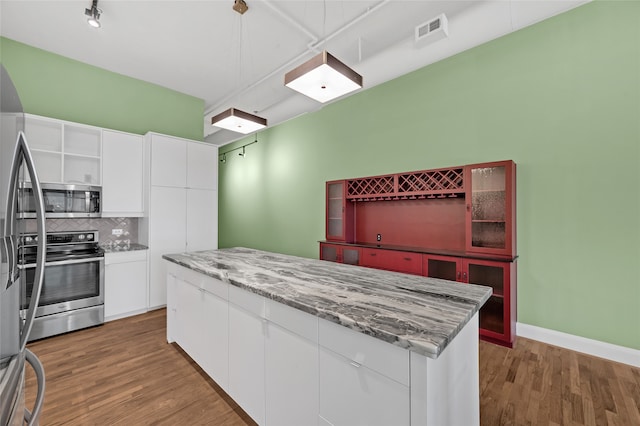 kitchen with white cabinetry, stainless steel appliances, tasteful backsplash, wood-type flooring, and a kitchen island