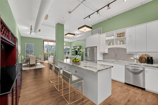 kitchen with a center island, light hardwood / wood-style flooring, appliances with stainless steel finishes, light stone counters, and white cabinetry