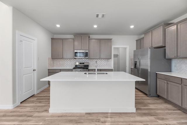 kitchen with a center island with sink, sink, appliances with stainless steel finishes, and light hardwood / wood-style flooring