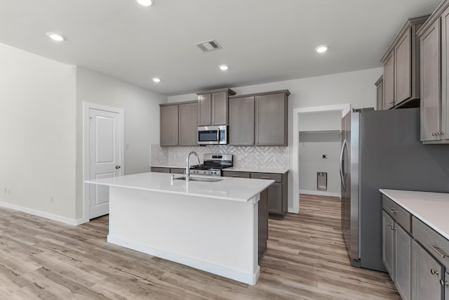 kitchen with sink, stainless steel appliances, tasteful backsplash, light hardwood / wood-style floors, and a center island with sink