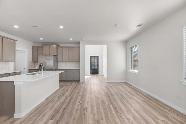 kitchen with sink, decorative backsplash, a large island, light hardwood / wood-style floors, and stainless steel fridge with ice dispenser