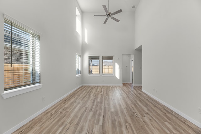 unfurnished living room featuring ceiling fan, a wealth of natural light, a towering ceiling, and light wood-type flooring