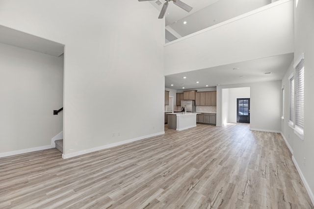 unfurnished living room with ceiling fan, high vaulted ceiling, and light hardwood / wood-style floors