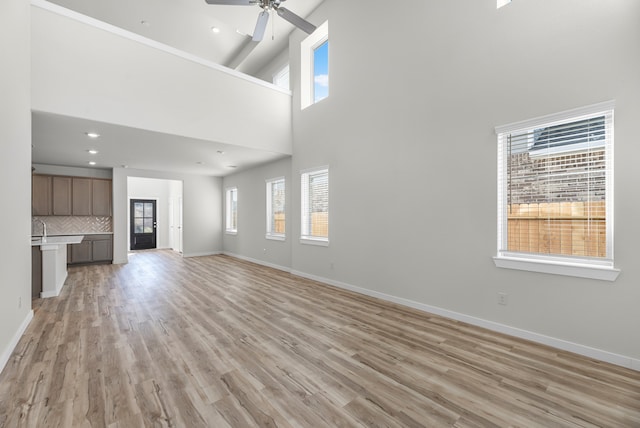 unfurnished living room with ceiling fan, light wood-type flooring, and a high ceiling