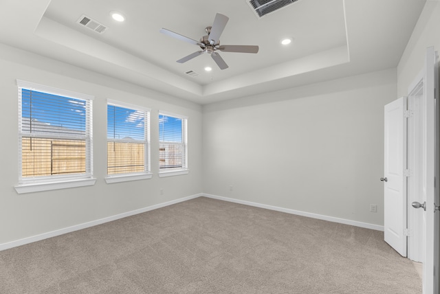 carpeted spare room featuring plenty of natural light, ceiling fan, and a tray ceiling