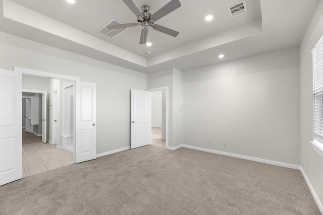 unfurnished bedroom featuring a tray ceiling, ceiling fan, and light carpet