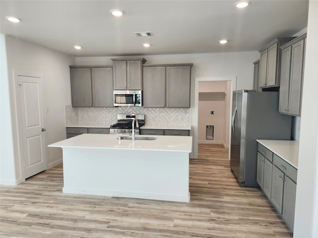 kitchen with appliances with stainless steel finishes, gray cabinetry, a kitchen island with sink, sink, and light hardwood / wood-style flooring