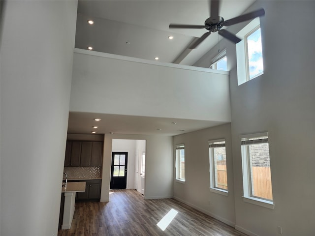 unfurnished living room featuring ceiling fan, a towering ceiling, and dark wood-type flooring