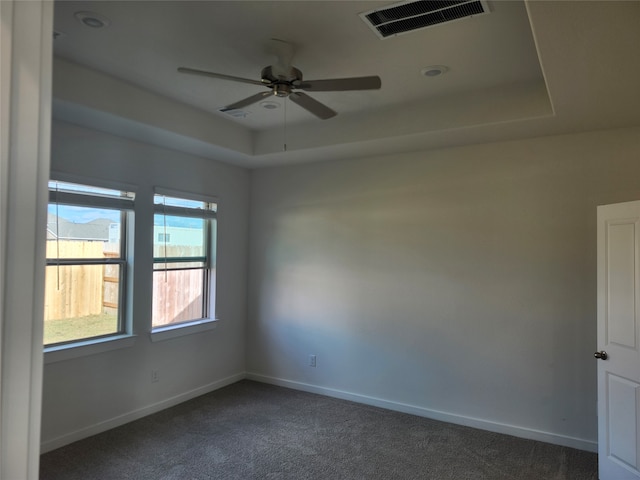 spare room with ceiling fan, dark carpet, and a tray ceiling