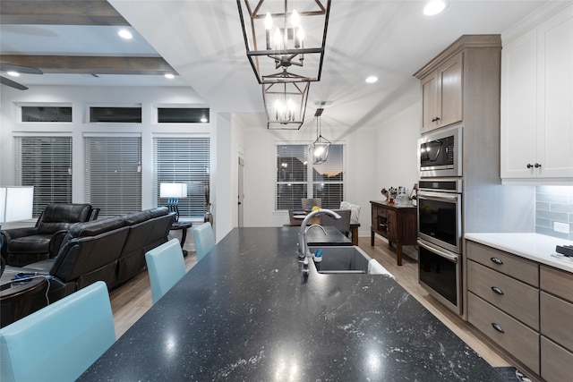 kitchen featuring appliances with stainless steel finishes, sink, pendant lighting, beamed ceiling, and light hardwood / wood-style floors