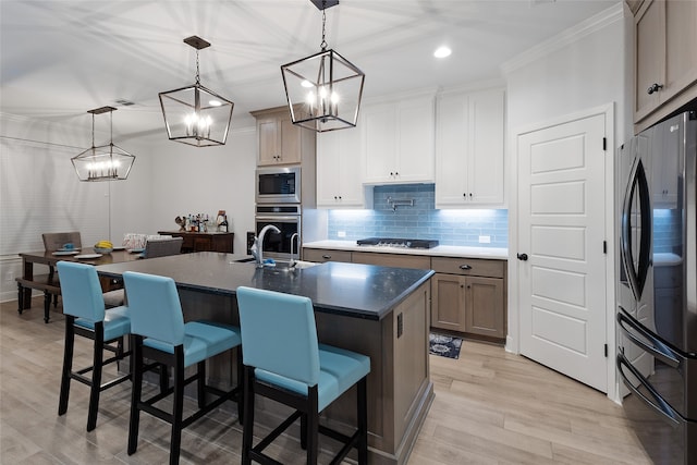 kitchen featuring hanging light fixtures, appliances with stainless steel finishes, an island with sink, white cabinets, and light wood-type flooring