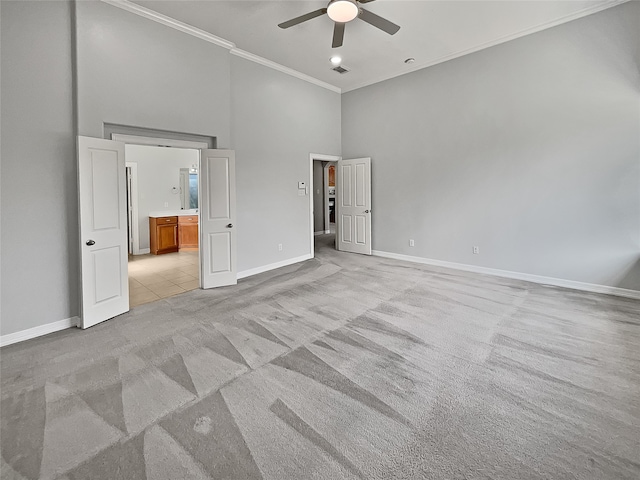 unfurnished bedroom featuring a towering ceiling, ornamental molding, light colored carpet, ceiling fan, and connected bathroom