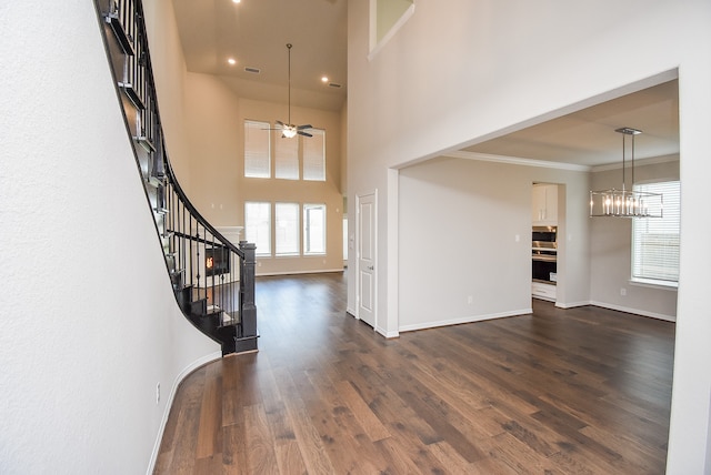 entryway with dark hardwood / wood-style floors, crown molding, ceiling fan with notable chandelier, and a high ceiling