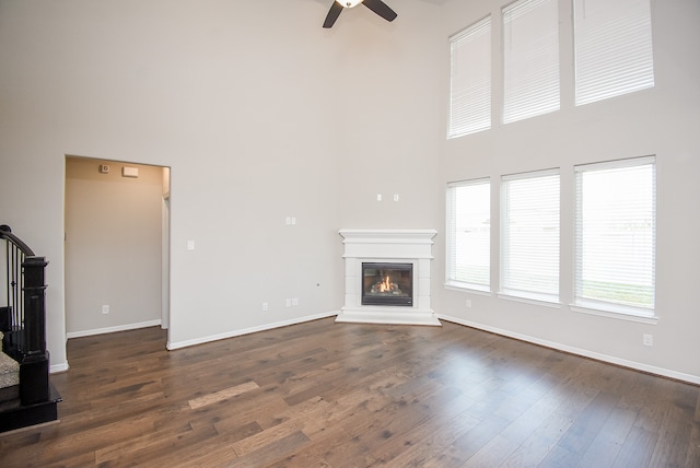 unfurnished living room featuring a towering ceiling, ceiling fan, and dark wood-type flooring