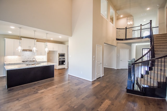 kitchen featuring a kitchen island with sink, a high ceiling, white cabinets, hanging light fixtures, and dark hardwood / wood-style flooring