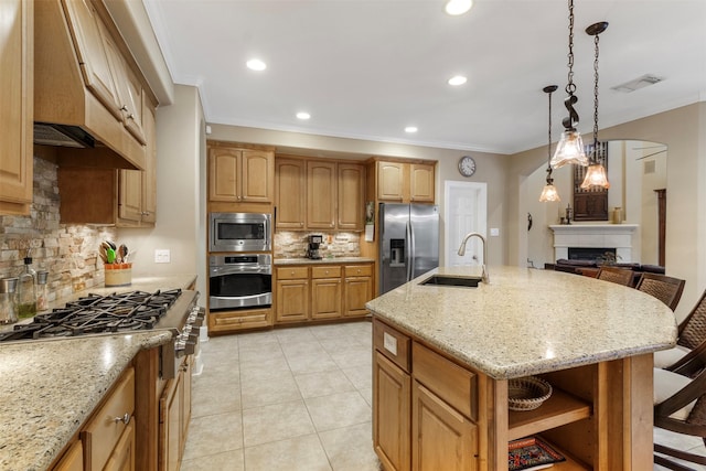 kitchen featuring an island with sink, a tiled fireplace, decorative backsplash, appliances with stainless steel finishes, and sink