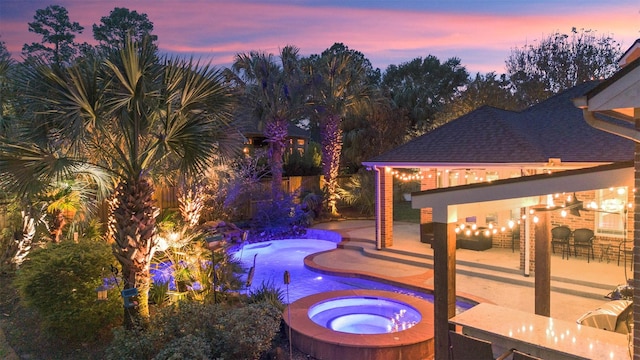 pool at dusk featuring a patio and an in ground hot tub