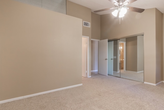 unfurnished bedroom with ceiling fan, a towering ceiling, light carpet, and a closet