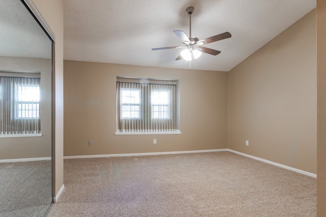 carpeted empty room featuring a wealth of natural light, ceiling fan, and a textured ceiling