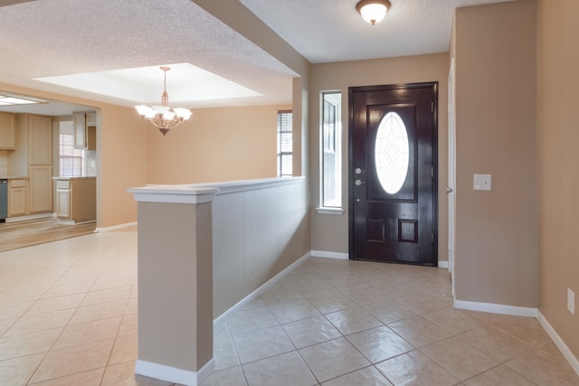 foyer with a tray ceiling, light tile patterned floors, a textured ceiling, and an inviting chandelier