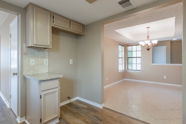 kitchen featuring a raised ceiling, cream cabinets, decorative light fixtures, an inviting chandelier, and light hardwood / wood-style flooring