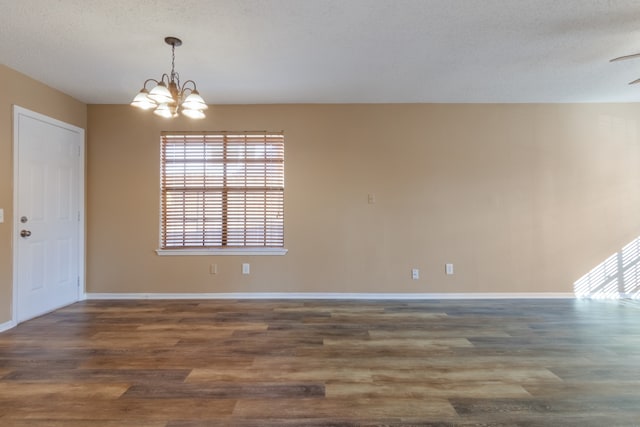 empty room with a chandelier, dark wood-type flooring, and a textured ceiling