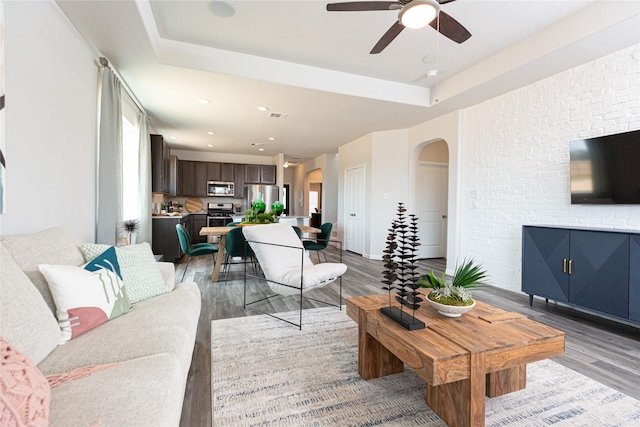 living room featuring ceiling fan, a raised ceiling, and light wood-type flooring