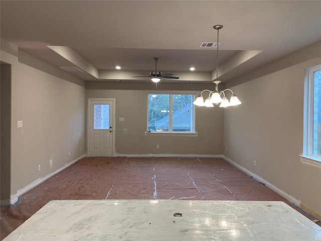 empty room with a raised ceiling and ceiling fan with notable chandelier