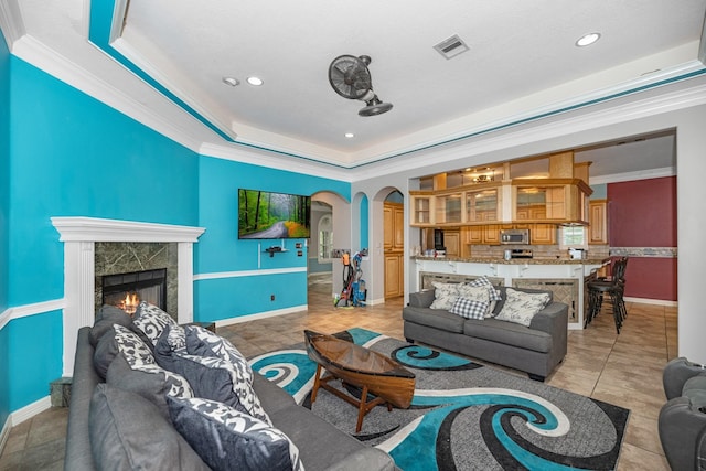 living room featuring a fireplace, light tile patterned floors, a raised ceiling, and crown molding