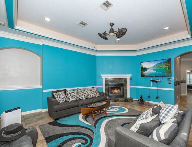 living room featuring a high end fireplace, crown molding, ceiling fan, a textured ceiling, and a tray ceiling