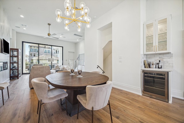 dining room with ceiling fan with notable chandelier, light hardwood / wood-style flooring, and wine cooler